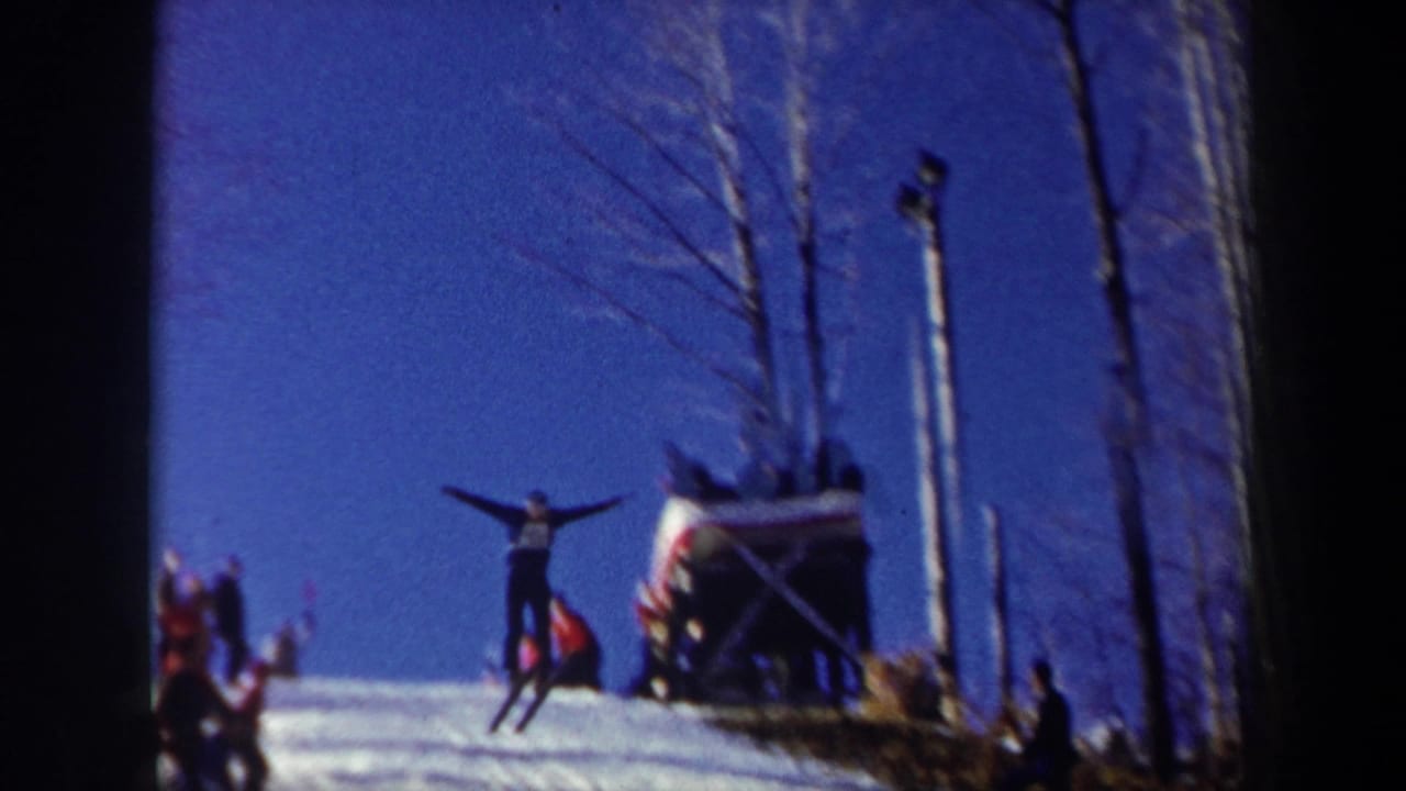 Skier is airborne near a jump with spectators and a platform nearby.