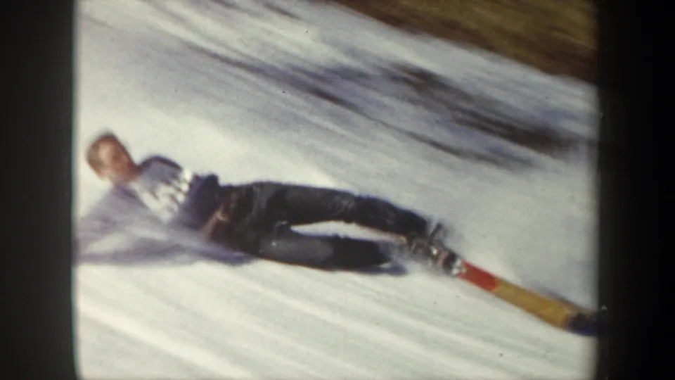 1962 New York home-movie frame showing the skier down on the snow after the jump, with long skis stretched across the slope.