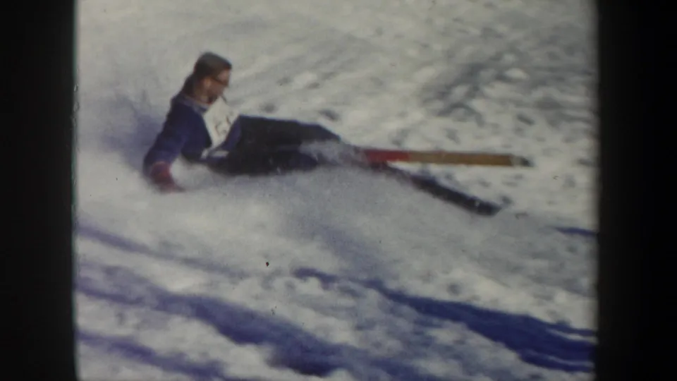 1962 New York 8mm frame showing the fallen skier resting in the snow after the jump, with one ski stretched across the foreground.