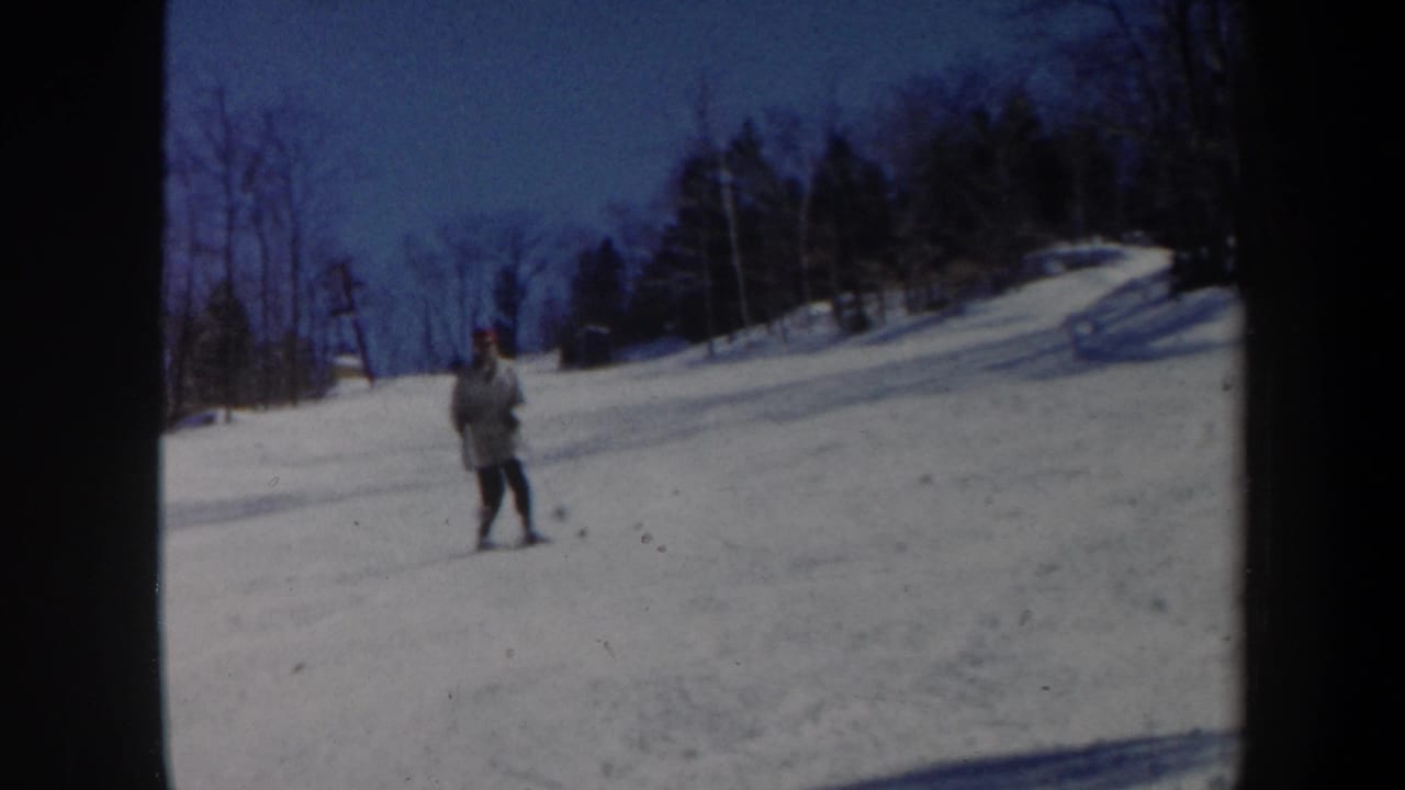1962 Vermont home-movie frame showing a skier in a red hat on a snowy hillside bordered by bare trees.