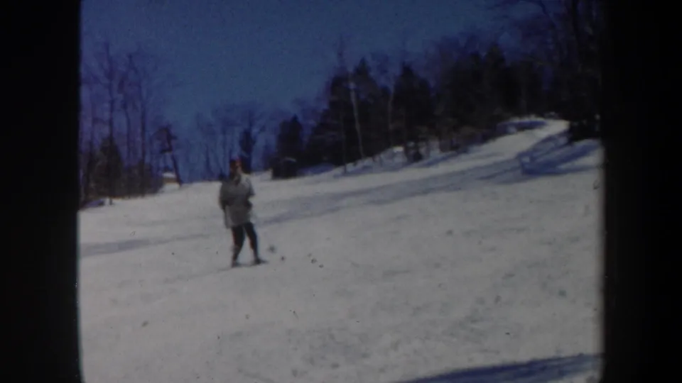 1962 Vermont home-movie frame showing a skier in a red hat on a snowy hillside bordered by bare trees.