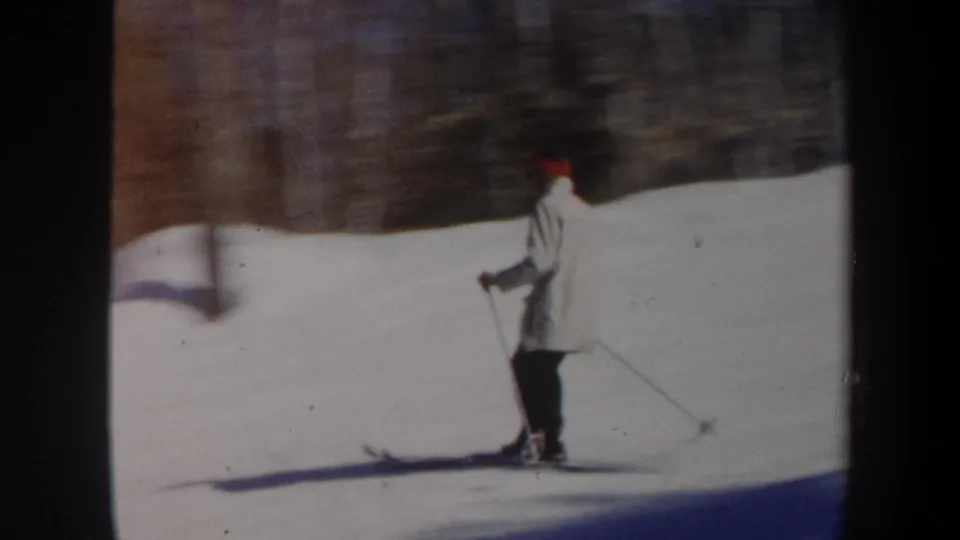 Profile view of the skier on a Vermont snow slope, with trees blurred behind in the 8mm frame.