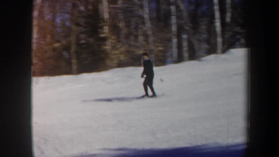 1962 Vermont 8mm frame showing a dark-clothed skier on an open snow slope with winter woods behind.
