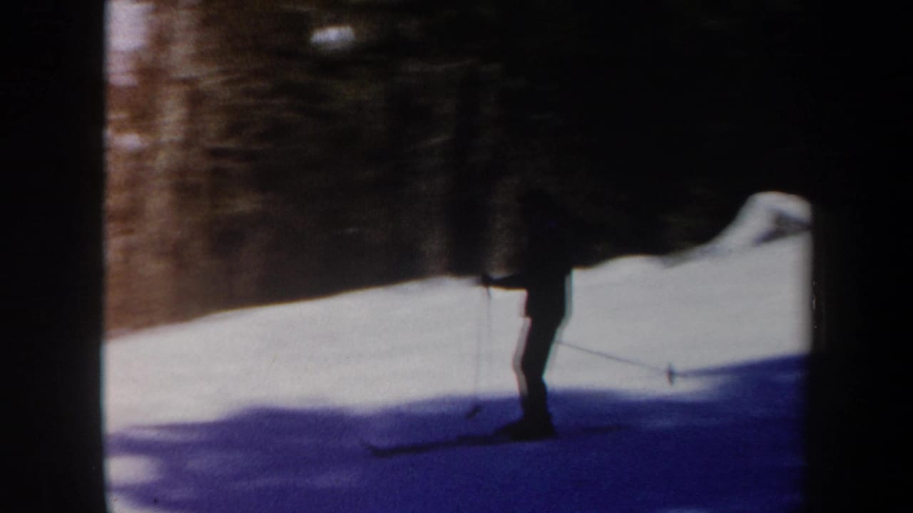 Skier crosses a snow-covered slope beside wooded terrain.