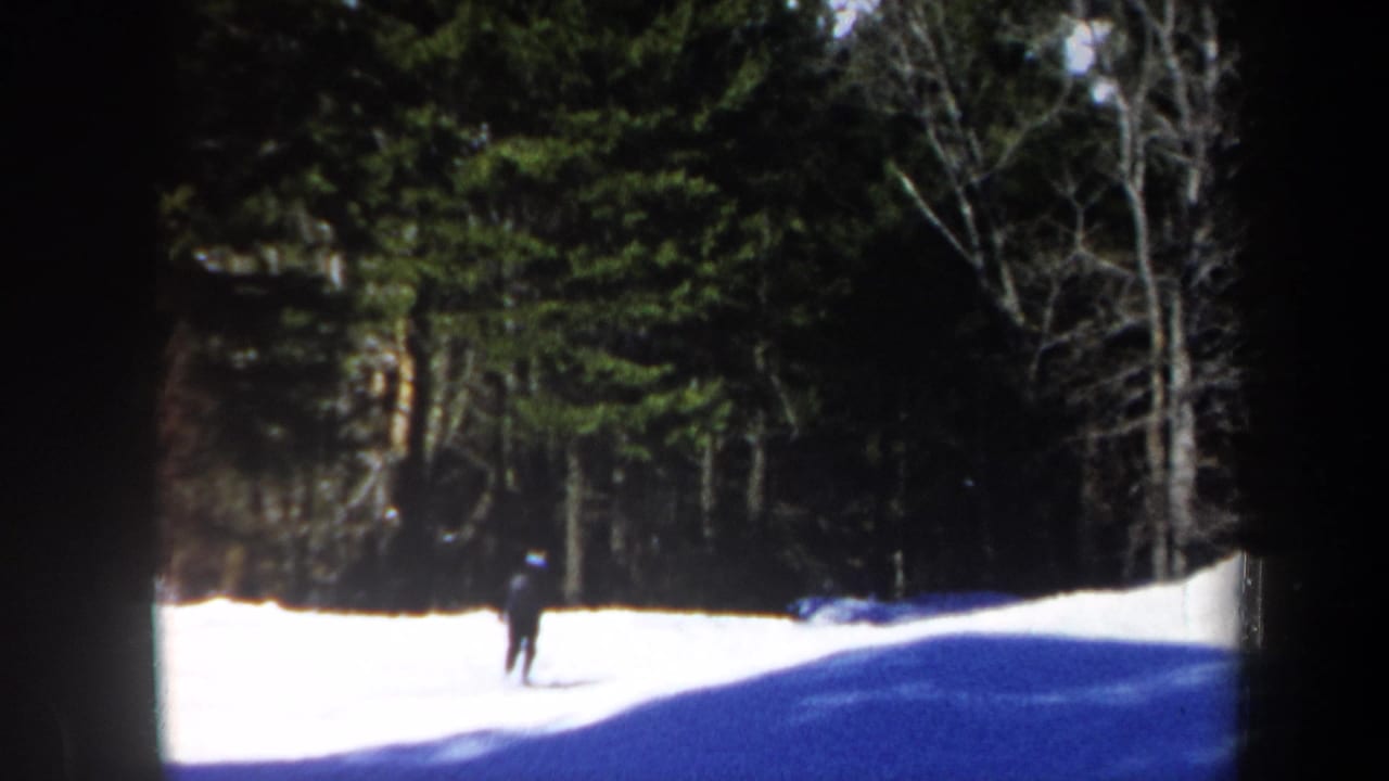 1962 Vermont 8mm frame showing a distant skier crossing a snowy clearing bordered by evergreen and bare trees.