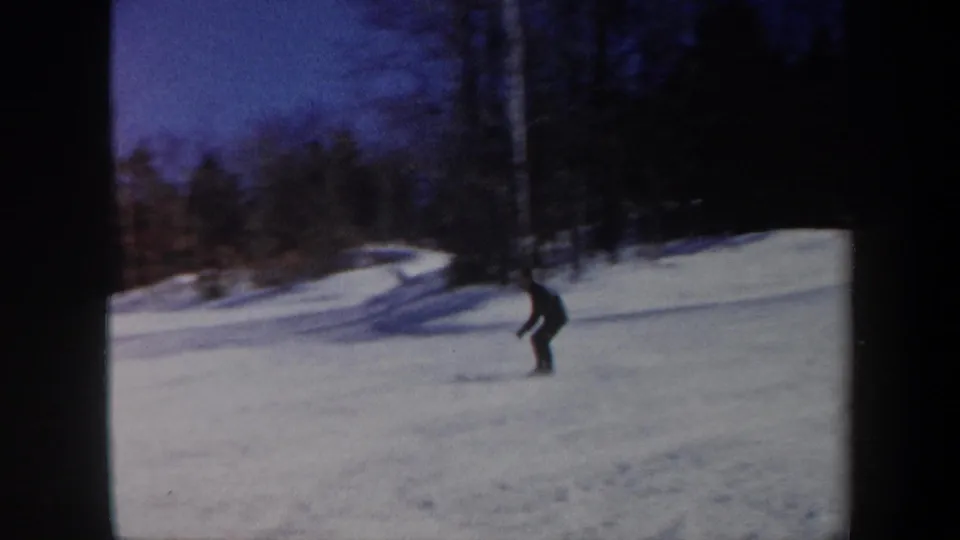 1962 Vermont 8mm frame showing a lone skier near the forest edge in a snowy clearing with blue shadows.
