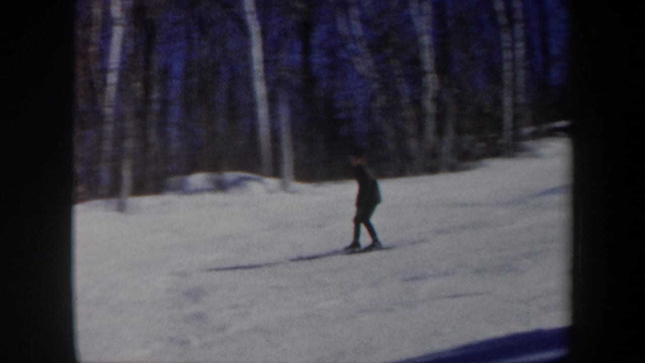 1962 Vermont home-movie frame with a distant skier moving through a quiet snowy forest clearing.