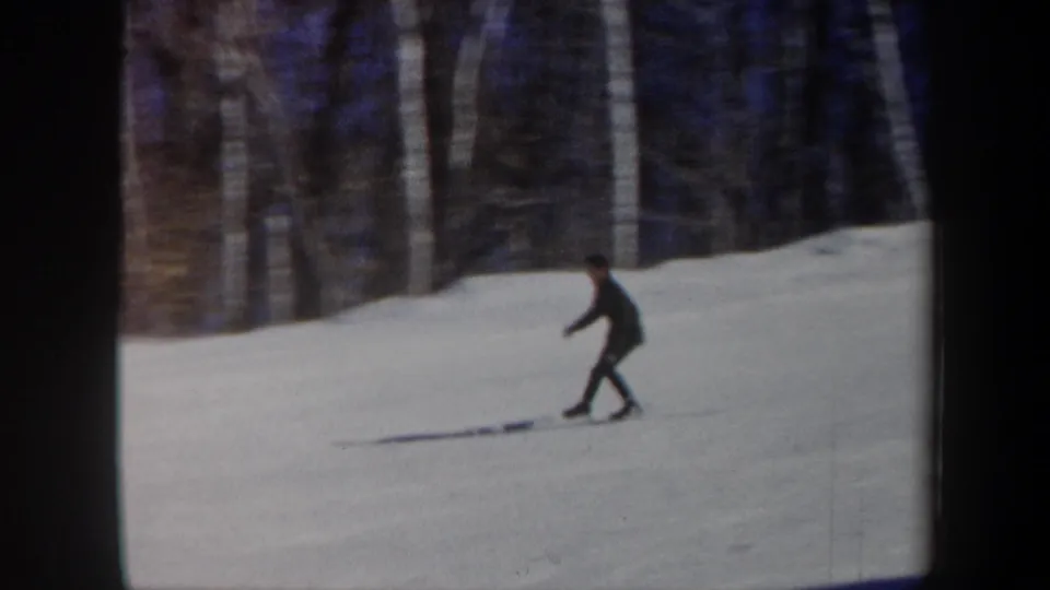 1962 Vermont 8mm frame showing a skier in dark winter clothes traversing a snowy slope near woods.