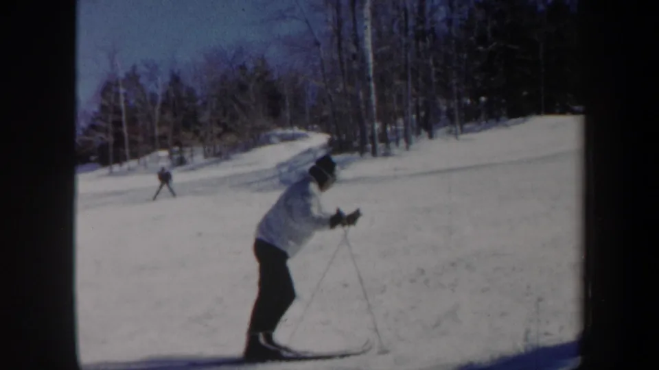 1962 Vermont home-movie frame of a skier leaning forward on a snowy track, surrounded by winter trees.