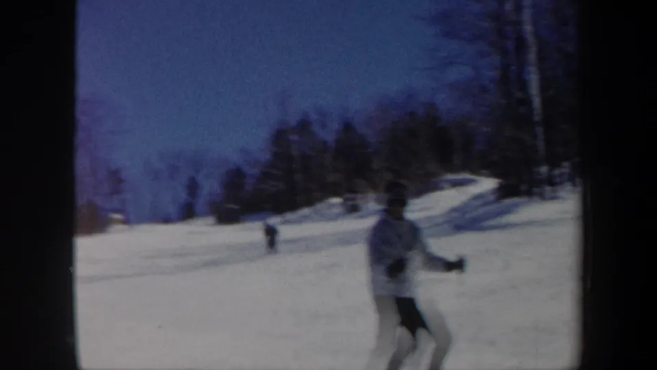 1962 Vermont ski frame showing a skier near the camera with a snowy open slope and trees beyond.