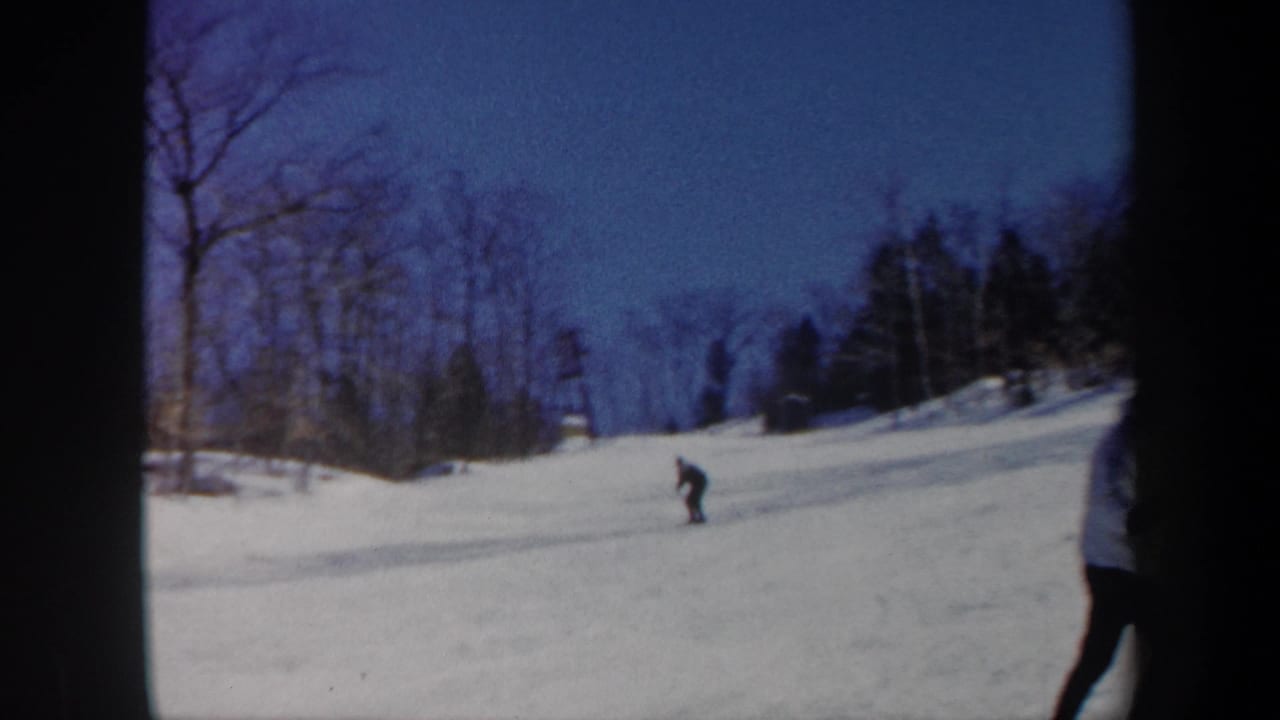 1962 Vermont 8mm frame showing a distant skier moving downhill across snow below bare winter trees.