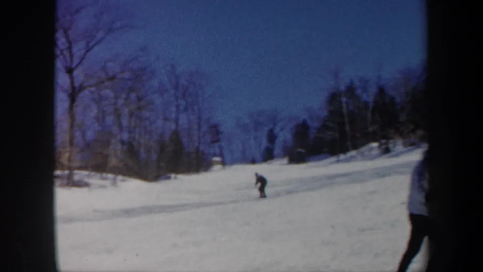 1962 Vermont 8mm frame showing a distant skier moving downhill across snow below bare winter trees.