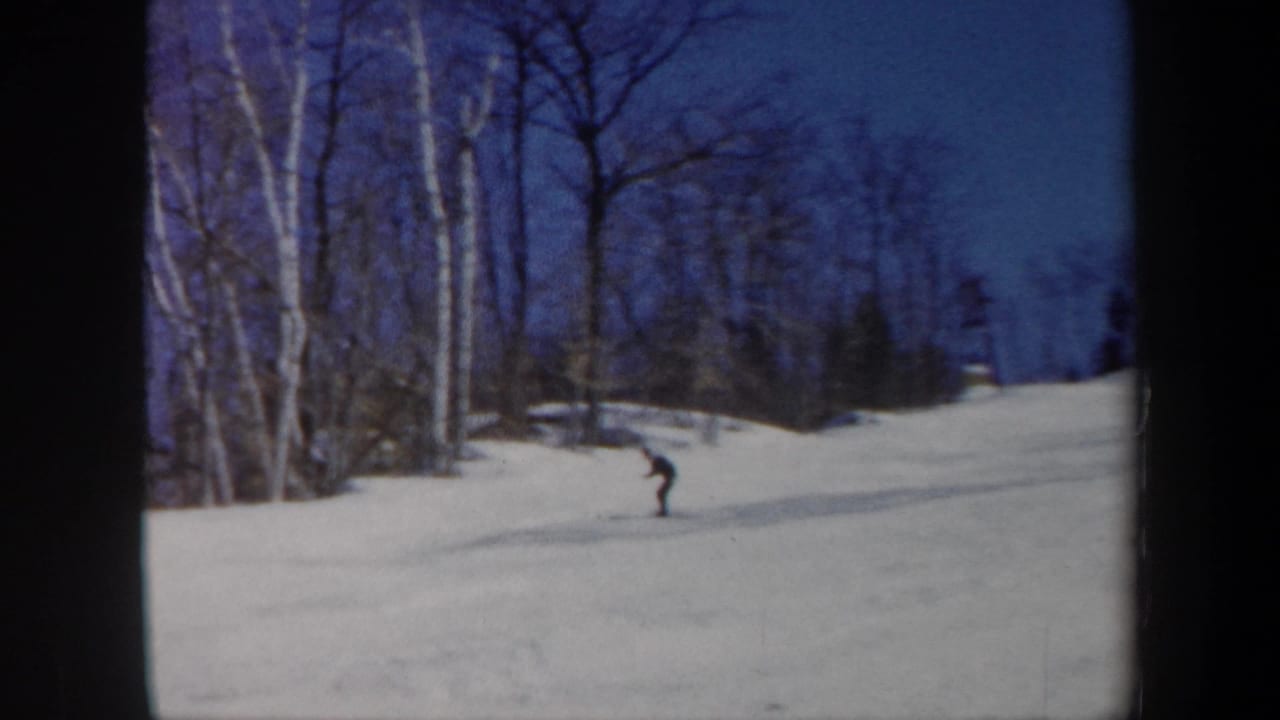 1962 Vermont home-movie frame with a skier on the slope and a partly cropped person watching near the foreground edge.