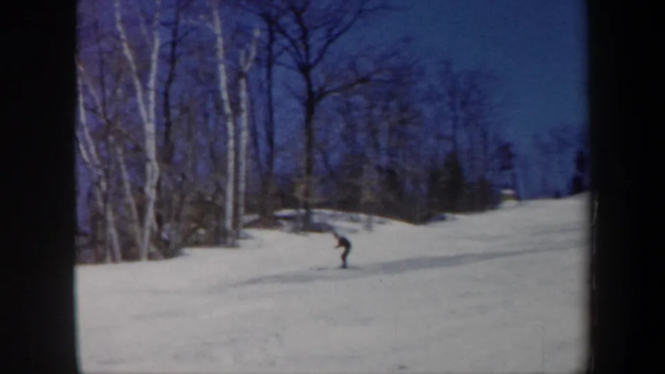1962 Vermont home-movie frame with a skier on the slope and a partly cropped person watching near the foreground edge.
