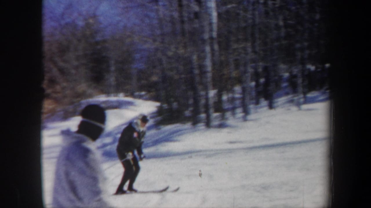 1962 Vermont 8mm frame showing a skier using poles on a snowy slope, with bare trees and another winter-clad figure nearby.