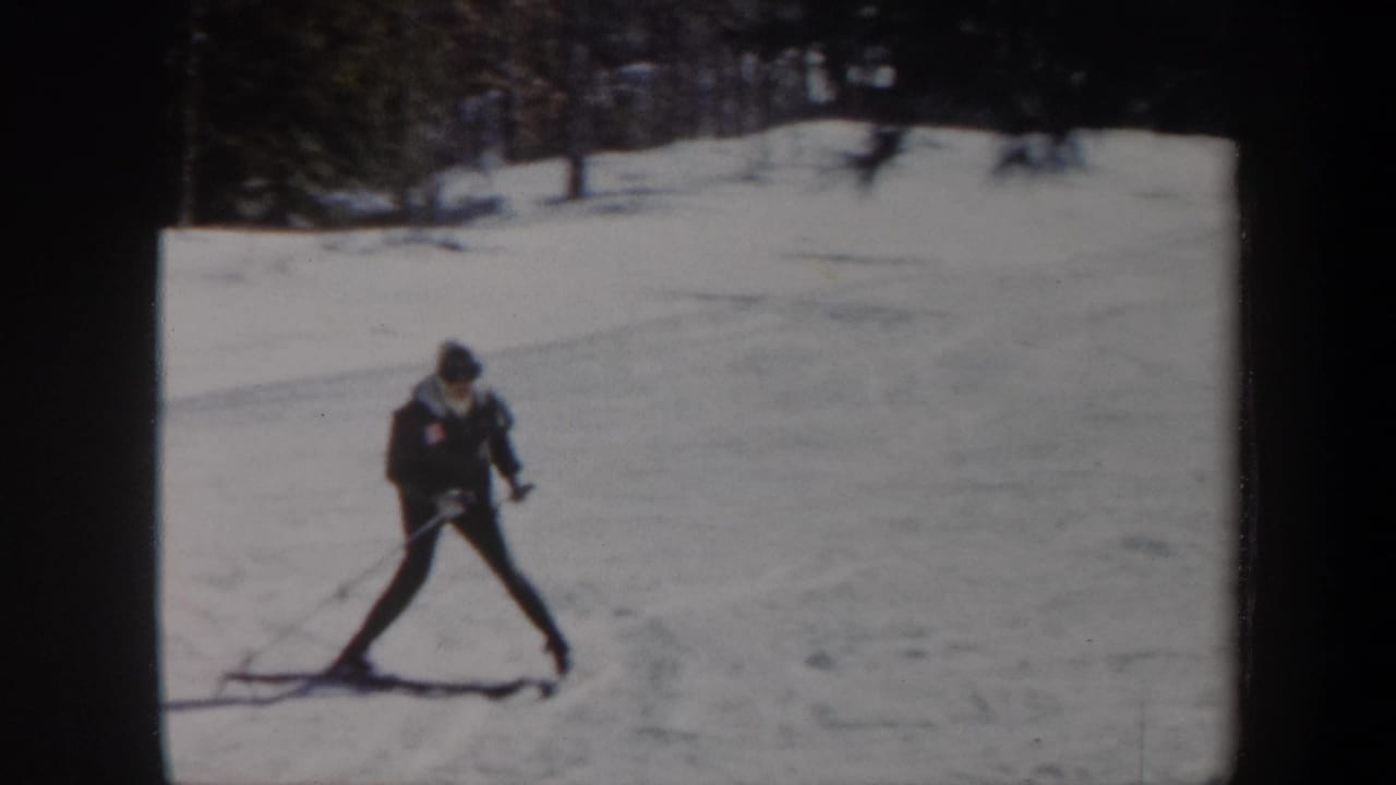 Skier glides across an open snowy area with poles extended and trees in the background.