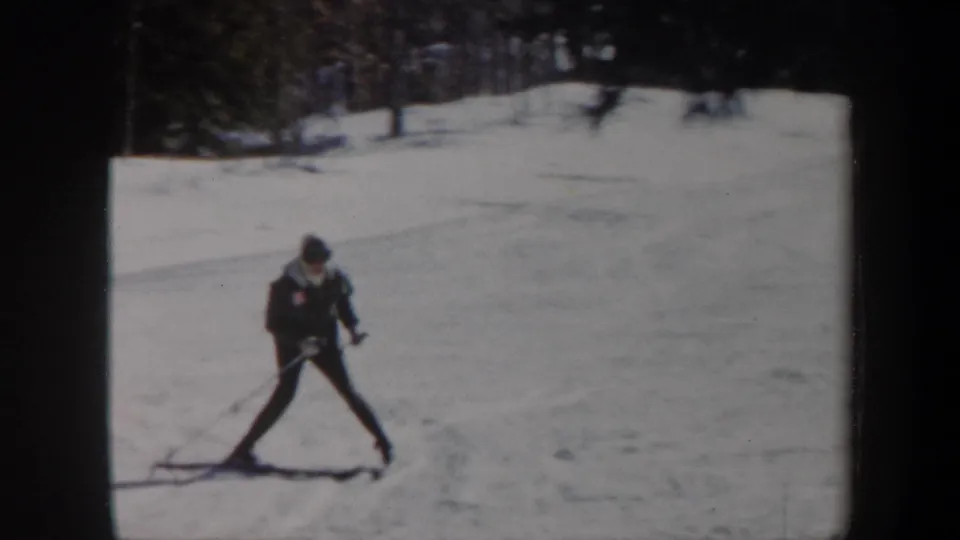 1962 Vermont home-movie frame of a cross-country skier in dark outerwear moving across a bright snowfield.