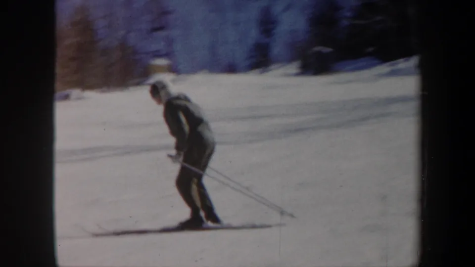 1962 Vermont home-movie frame of a skier leaning forward on cross-country skis, surrounded by snow and winter trees.