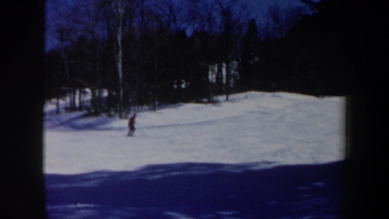 1962 Vermont 8mm frame showing a lone skier in red moving across a snow-covered slope below dark trees.