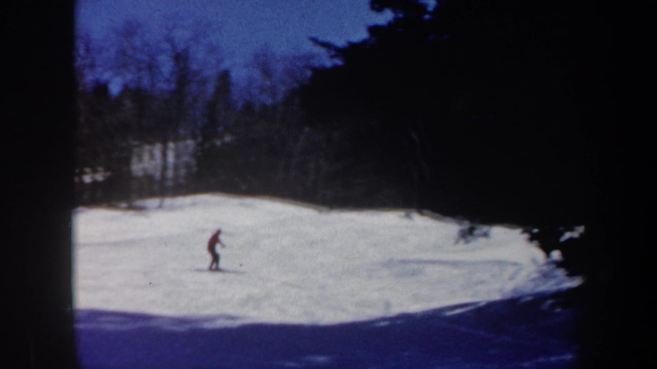 A distant skier moves across a Vermont snow slope in soft 8mm color, with woods and heavy vignetting around the frame.