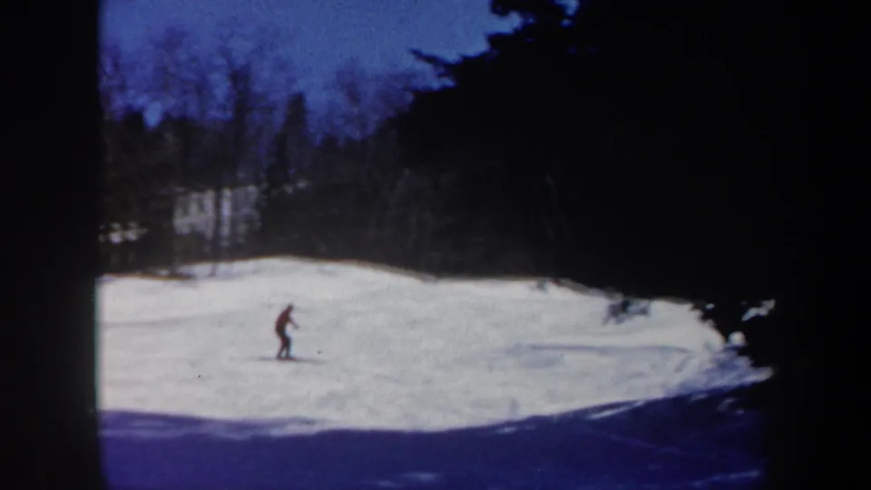 A distant skier moves across a Vermont snow slope in soft 8mm color, with woods and heavy vignetting around the frame.