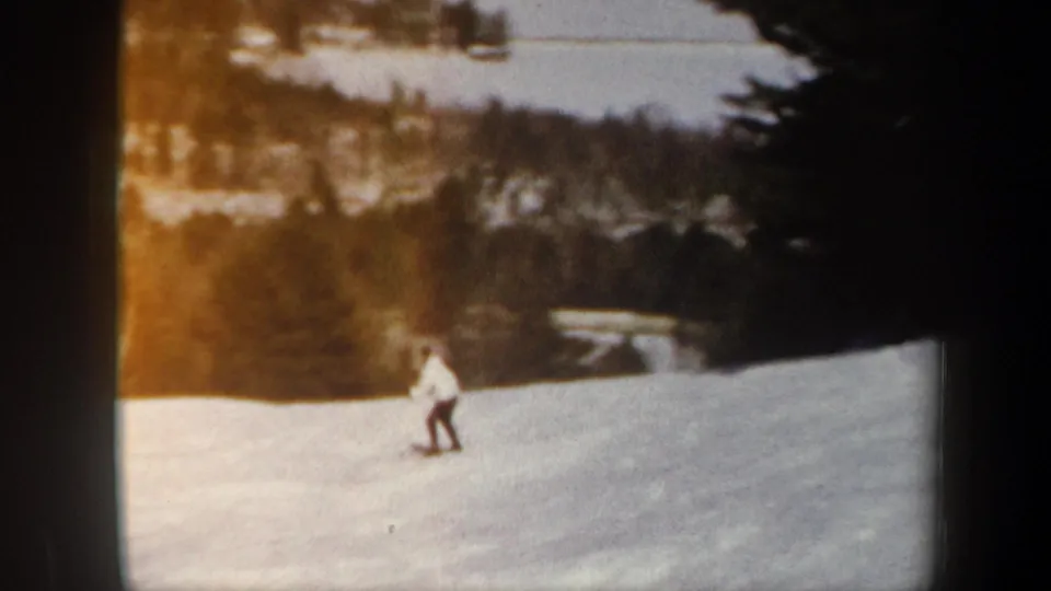 1962 Vermont frame showing a skier crossing an open snow slope, with winter trees and distant hills behind.