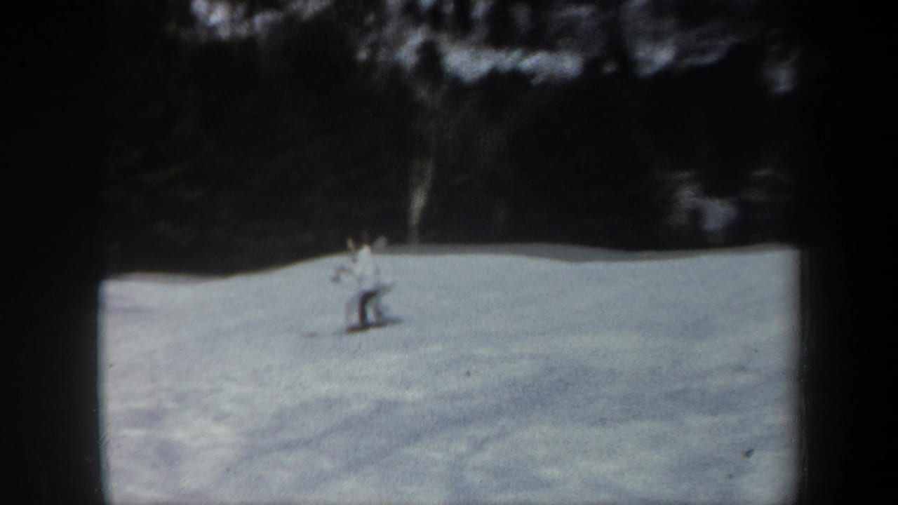Distant skier on a snowy Vermont slope in 1962 home-movie footage, with dark woodland behind the open snowfield.