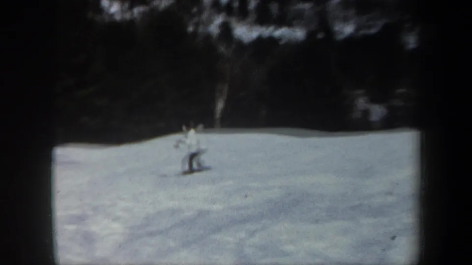 Distant skier on a snowy Vermont slope in 1962 home-movie footage, with dark woodland behind the open snowfield.