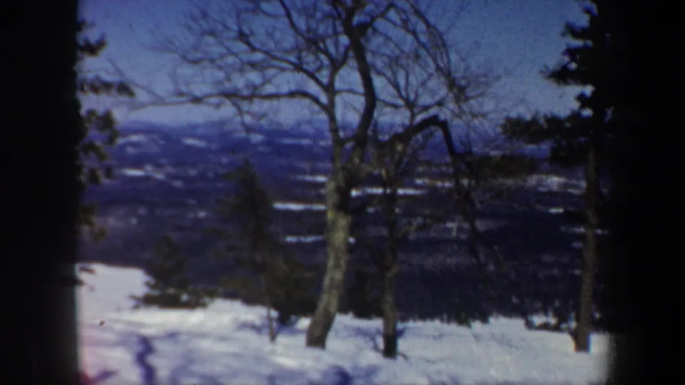 Snow-covered Vermont hillside with bare trees in the foreground and distant hills under a blue winter sky.