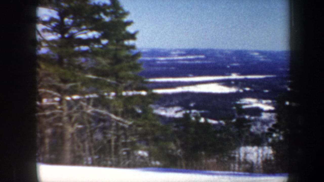 1962 Vermont 8mm frame showing a snow-covered valley beyond evergreen trees under a clear blue sky.