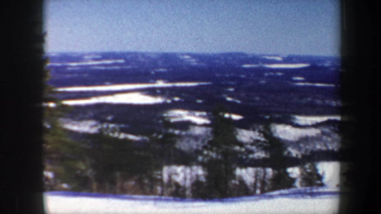 1962 Vermont home-movie view across a broad snowy valley, with wooded hills and dark 8mm frame borders.