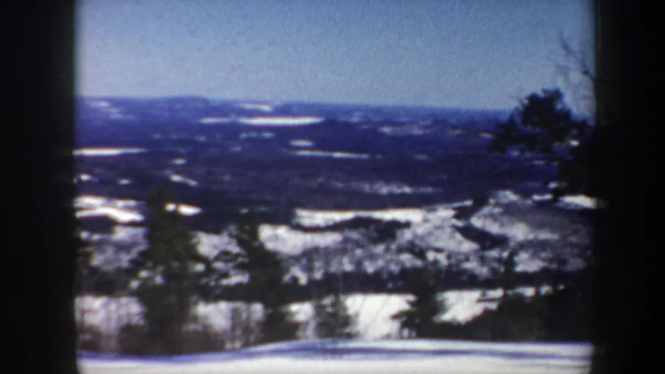 1962 Vermont 8mm frame of a winter valley panorama, with snowfields, distant hills, and trees near the lens.