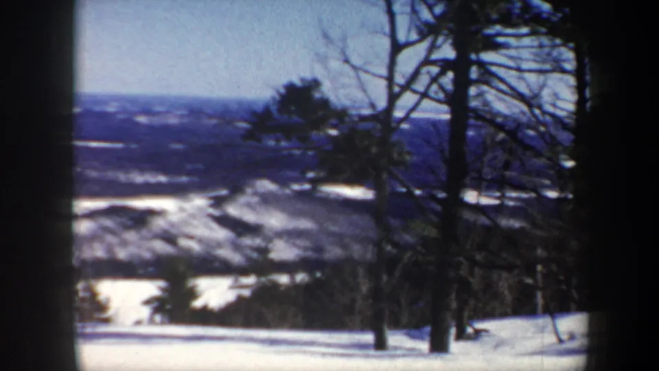 1962 Vermont home-movie frame showing bare trees on a snowy overlook above a distant winter valley.