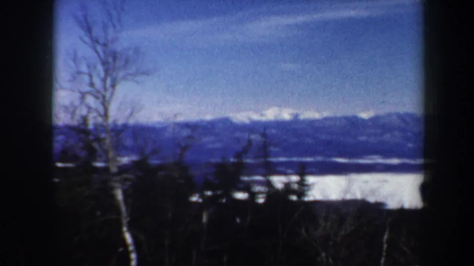 1962 Vermont 8mm frame emphasizing the snowy landscape, bare trees, blue sky, and distant mountain ridge.