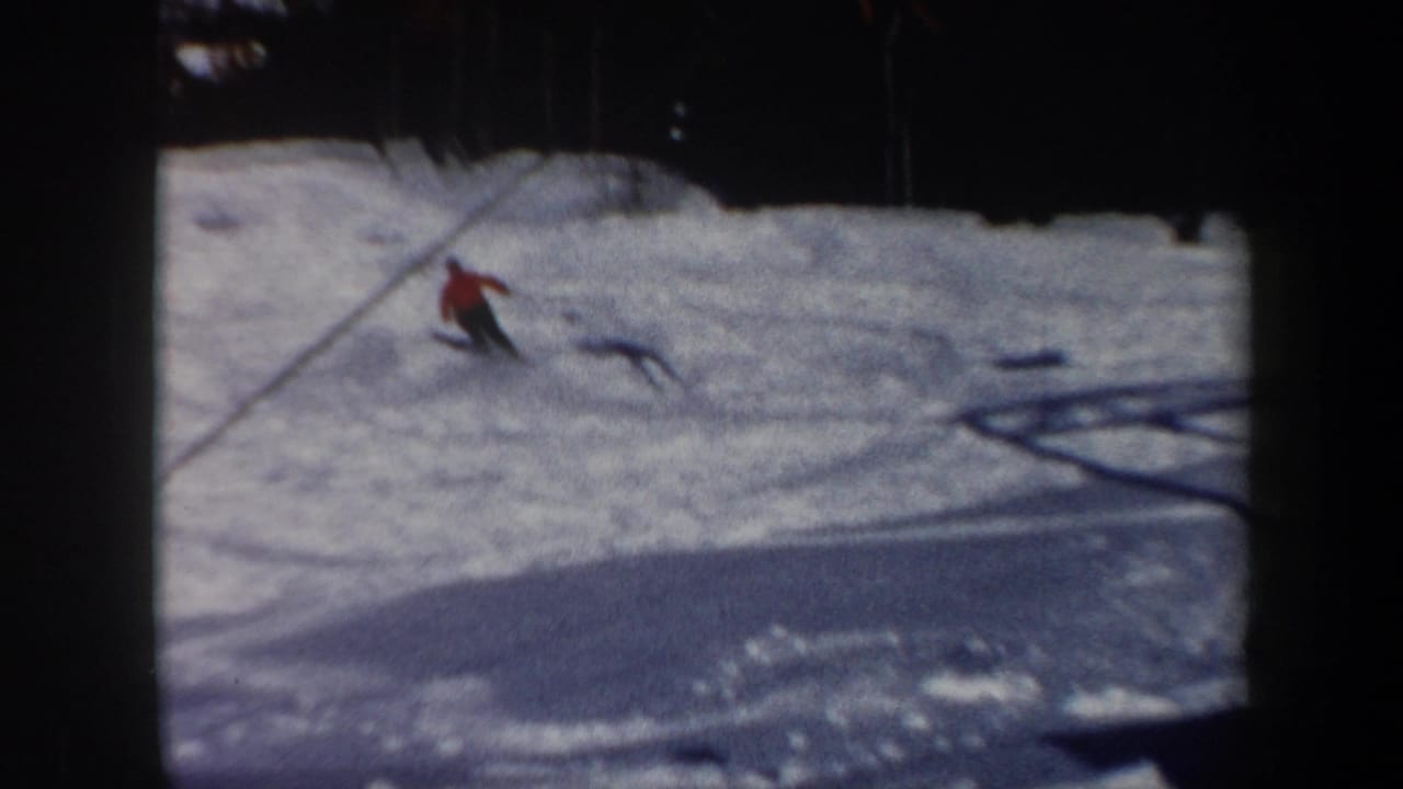 Skier in a red jacket descends a snowy slope near a visible lift cable.