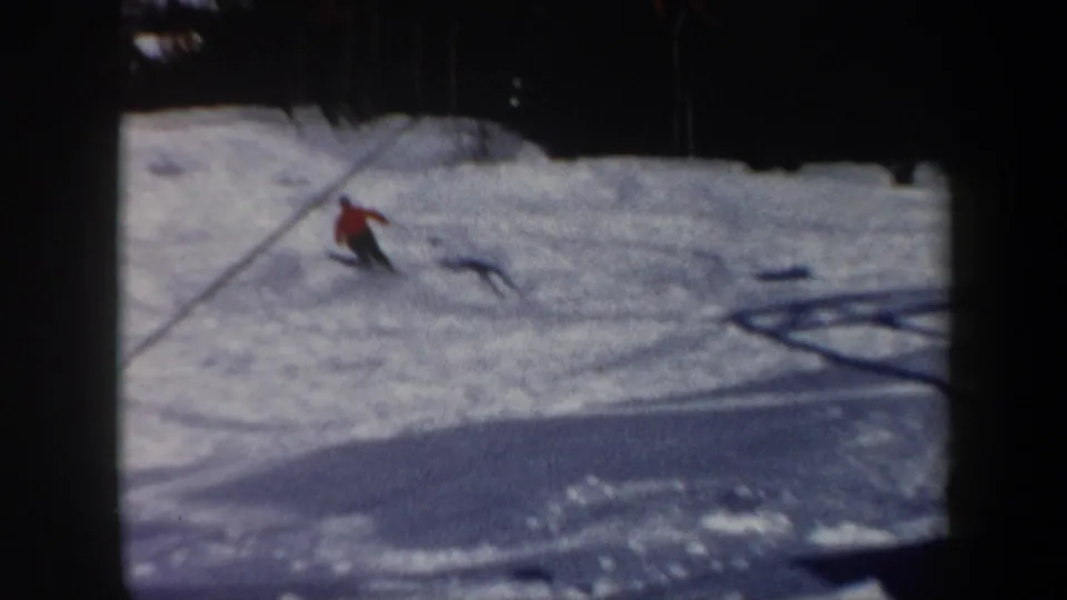 Vermont 1962 frame of a distant skier in a red jacket moving downhill across a snowy ski slope with a lift cable in view.