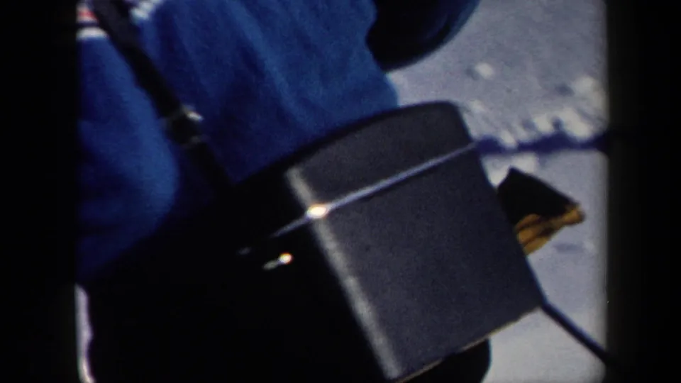 Close handheld 8mm frame of a skier in blue clothing and gear, cropped tightly as the camera catches movement on the snowy slope.
