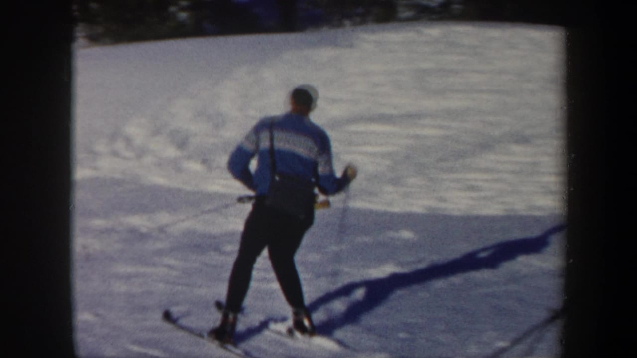 Skier seen from behind gliding downhill across bright snow.