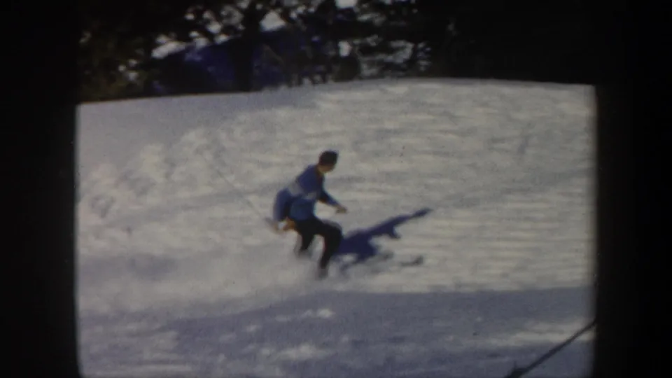 A distant view shows the adult skier leaning into the descent on a snow-covered Vermont hillside in 1962 footage.