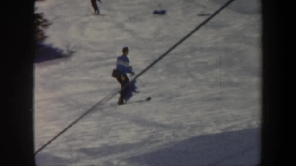 The skier moves across the snow near a diagonal line or shadow, with the 8mm frame showing soft focus and dark edges.