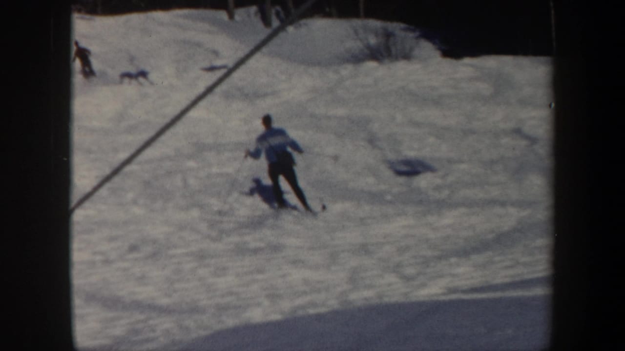 1962 Vermont 8mm frame showing a skier in a light and blue jacket moving downhill on a snowy slope with other skiers in the distance.