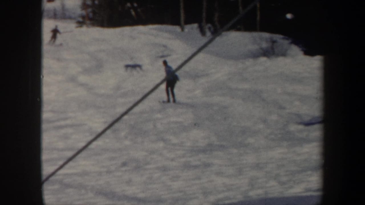 Distant skier on a snowy slope near a diagonal lift line and other small figures.