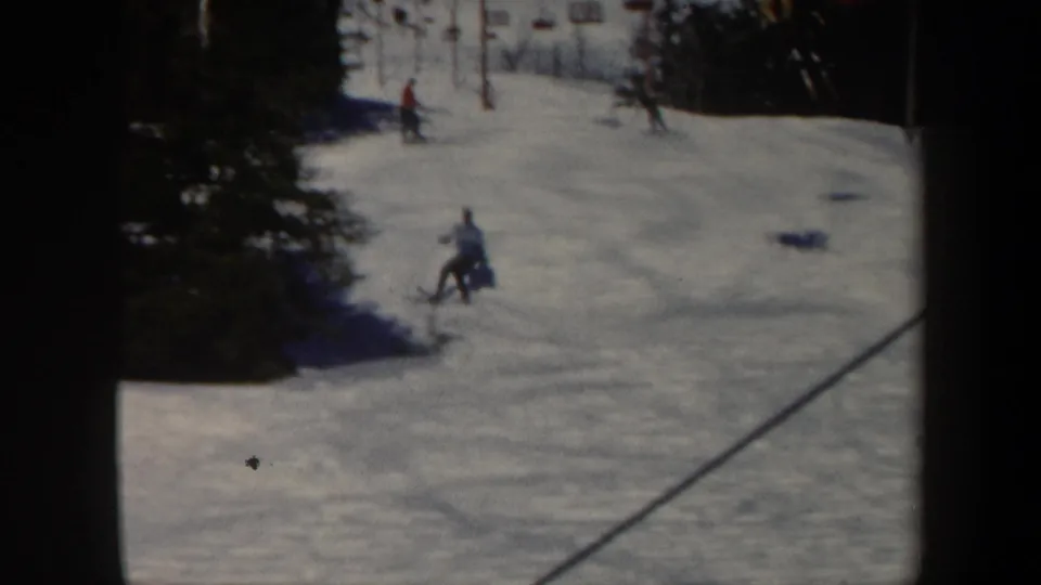 1962 Vermont home-movie frame showing a skier turning downhill beside evergreen trees, with other skiers farther up the snowy slope.