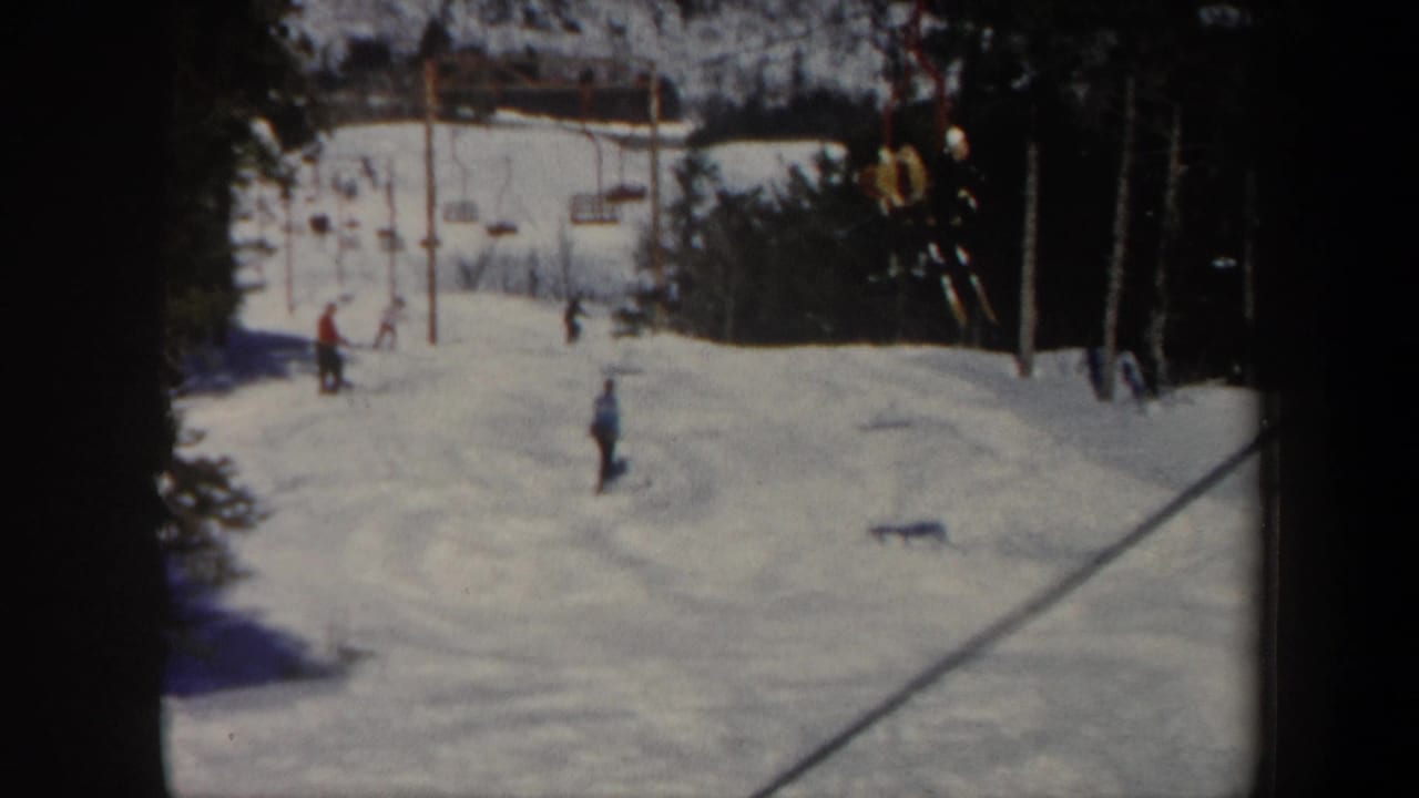 1962 Vermont 8mm frame showing skiers on a snowy slope near chairlift towers and dark evergreen trees.