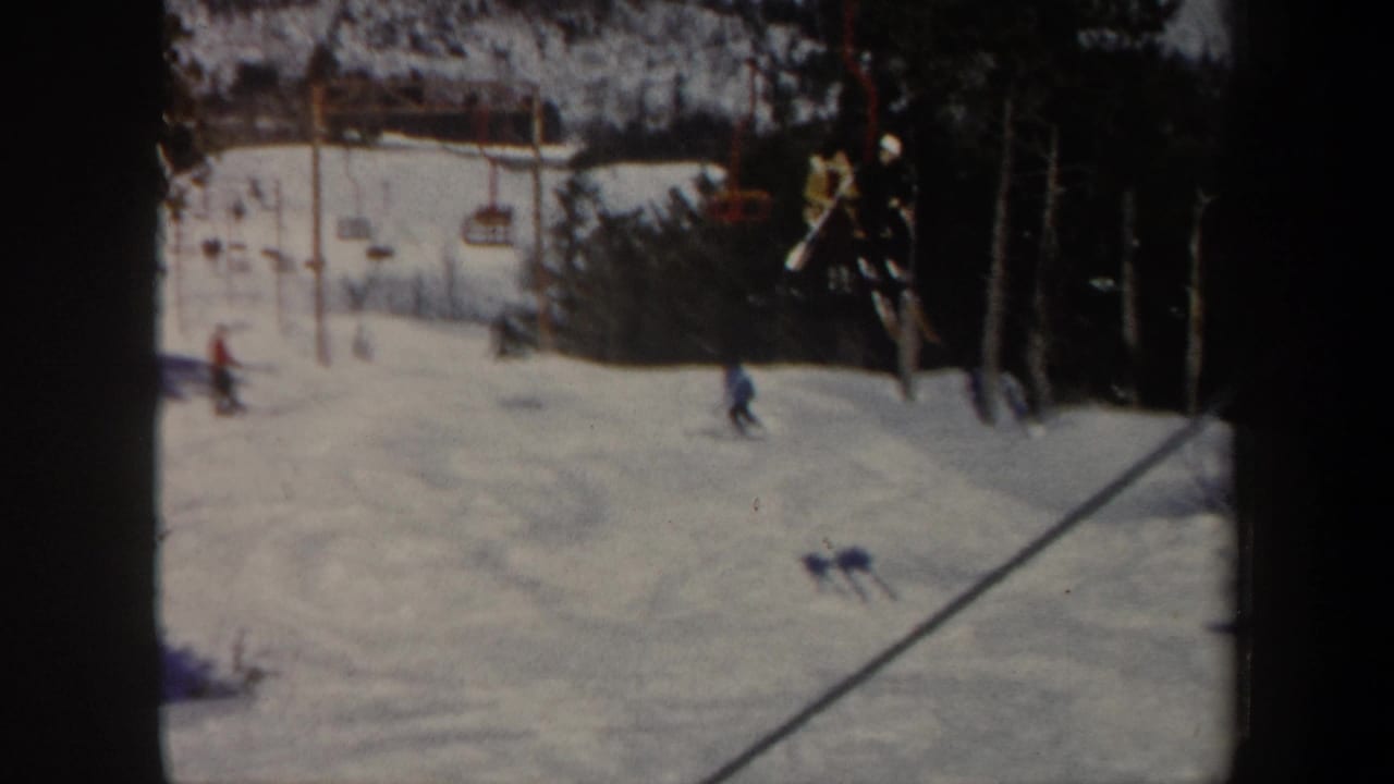 Several skiers descend a snowy run with a chairlift crossing the background.