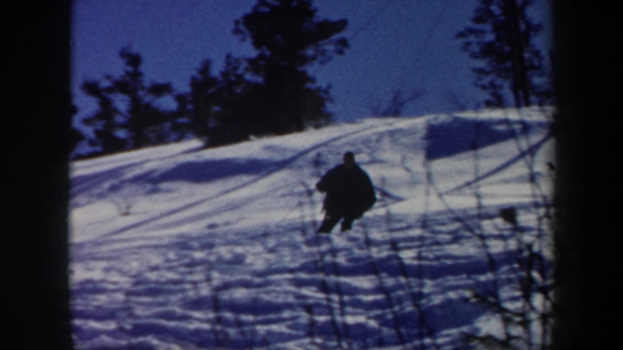 1962 Vermont 8mm frame showing a lone skier in dark winter clothing moving down a snowy wooded slope.