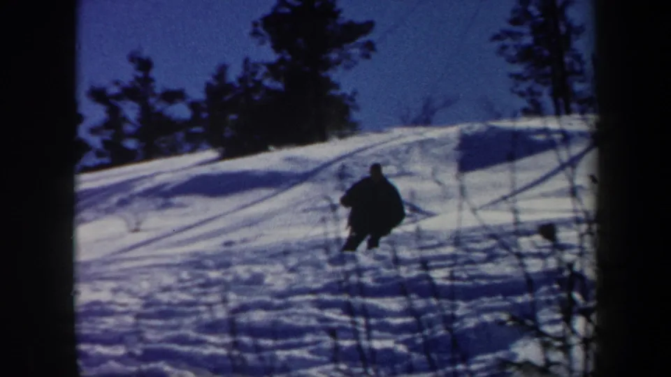 1962 Vermont 8mm frame showing a lone skier in dark winter clothing moving down a snowy wooded slope.