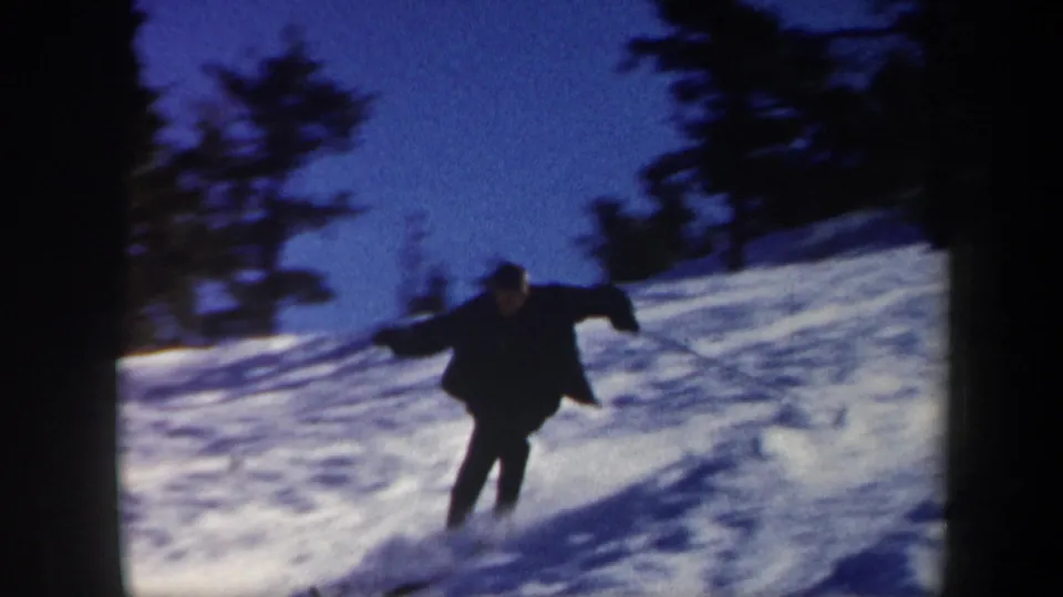 1962 Vermont 8mm still of a skier leaning through a turn on a wooded snowy hillside.