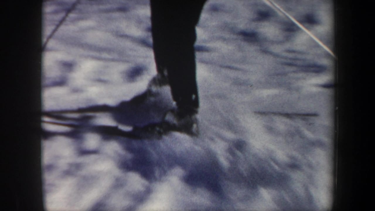 Close 8mm view of a skier's lower legs, skis, and poles gliding over snow in Vermont footage from 1962.