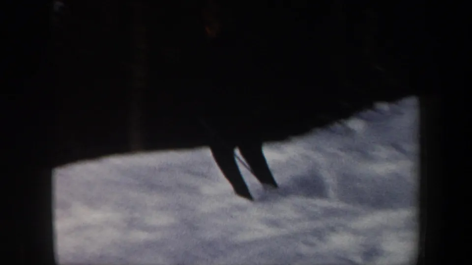 A silhouetted skier moves across a snow-covered slope, with soft 8mm exposure and heavy dark borders.